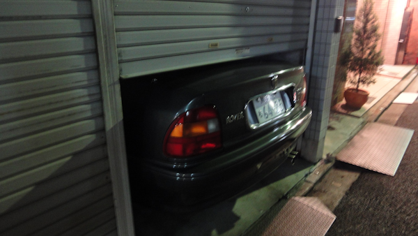 a garage door half-closed with the back end of a car sticking out